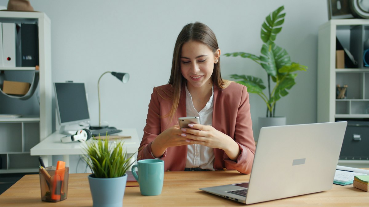 Impiegata alla scrivania che legge sul telefono le notifiche di TeamFluXit